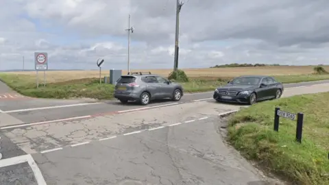 Google Google Street View image of a crossroads surrounded by farmland with two cars passing in opposite directions