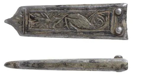 Andrew Williams/Norfolk County Council Two views of a medieval silver strap-end. It is rectangular in shape with a flat top, with two silver circles soldered at the top, narrowing slightly along its body until it ends in a point.  The front side is engraved with a human-headed bird. The other view is of its narrow side, wider at the top and narrower at the bottom