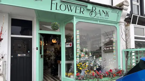 The entrance of the flower bank shop with flowers outside it