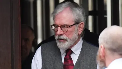 PA Media A man with a white beard and brown rimmed glasses looks off camera. He is wearing a white shirt, red tie and grey waistcoat. 