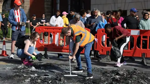 Reuters People help sweep up debris from a burnt vehicle after a night of violent anti-immigrant demonstrations in Sunderland