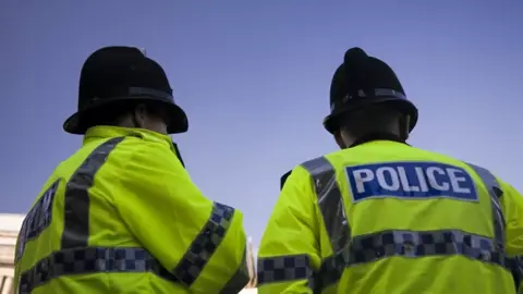 Two police officers in hi-vis jackets facing away from the camera.