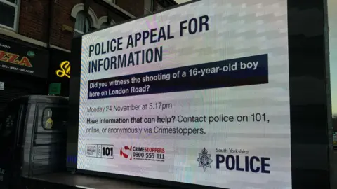 A mobile advertising board with the message, Police appeal for information. Did you witness the shooting of a 16-year-old boy here on London Road? Monday 24 November at 5.17pm.