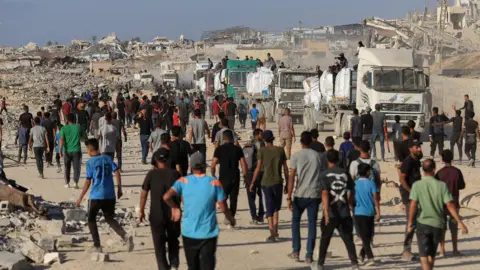 Os palestinos da Reuters se reúnem para coletar alimentos da Aid Forries guardados por membros armados de clãs locais em Beit Lahia, norte de Gaza (25 de junho de 2025)