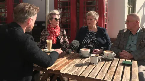 Political Editor for BBC East Midlands, Peter Saul interviews Jenni Oliver, Sue Saddington and Tony Roberts-  members of Robert Jenrick's local Conservative association in Newark - over coffee outdoors on a bench infront of iconic red telephone boxes  