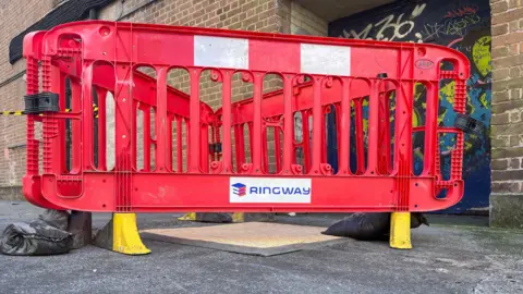 A view of the covered drain with a red barrier in front.