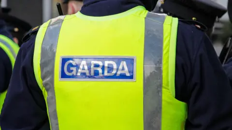  A Garda officer wears a yellow jacket with 'Garda' on the back in grey writing and blue background