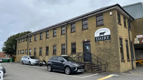 BBC Guernsey Dairy - A building with yellow walls and a sign that says Guernsey Dairy, with the black outline of a Guernsey cow on it. 