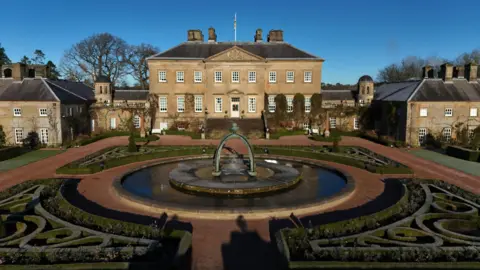 PA Media A view of Dumfries House with the gardens and a pond in the foreground on a sunny day with blue skies.