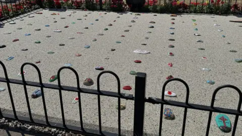 Brightly coloured pebbles are placed in resin in the ground surrounded by a short metal fence.