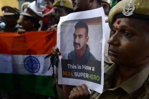 AFP Pasukan Keamanan India berpose dengan bendera nasional dan foto -foto pilot Angkatan Udara India Abhinandan Vanthaman selama acara untuk berdoa untuk kembalinya, di Kuil Kalikambal di Chennai pada 1 Maret 2019. Ribuan orang India, beberapa bendera melambai dan bernyanyi, dikumpulkan 1 Maret untuk memberikan sambutan pahlawan kepada seorang pilot angkatan udara yang akan dikembalikan ke seluruh perbatasan setelah ditembak jatuh oleh seorang pahlawan.