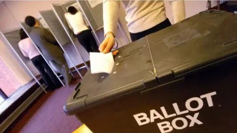 BBC A black ballot box with someone putting a voting slip in 