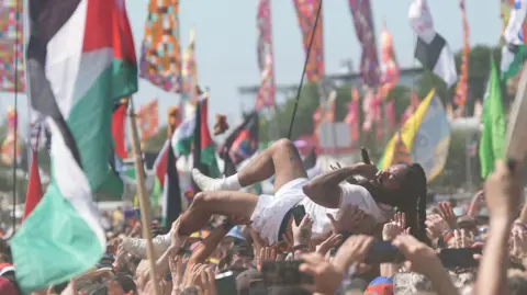 PA Media Bob Vylan crowd surfs during his performance.