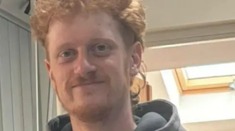 An image of Michael Cockburn-Hilton looking and smiling at the camera. He is wearing a hooded jacket and has ginger hair. 