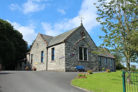 Billy McCrorie A small school in Dumfries and Galloway at the top of a curved driveway with a tidy grass lawn in front and tree growing