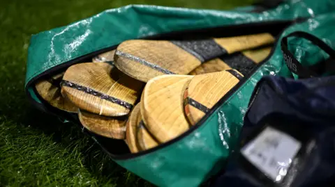 Getty Images A green kit bag full of hurleys sticks on grass.
