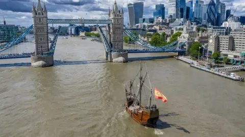 The Nao Santa María flagship sails toward Tower Bridge, which has its bascules raised.