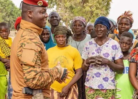 Ibrahim Traoré/X Ibrahim Traoré in military fatigues and red beret, with holstered gun visible, speaks to crowd, mainly made up of female farmers, who stand just in front of him