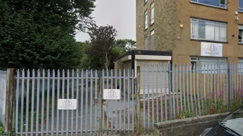 Google A large office-type building with a sharp-pointed metal fence around the front.