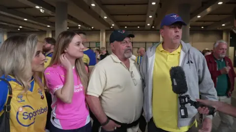 Two women and two men interviewed after the semi-final on Saturday at Wembley, in a crowd. Some are wearing the team's colours.