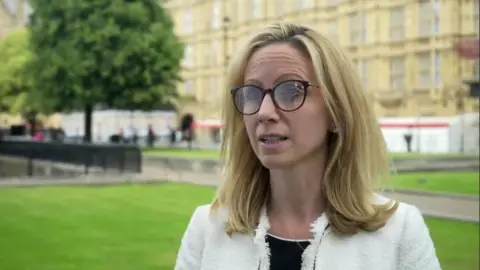 BBC Lucy Rigby with long blond hair and glasses standing in College Green, Westminster