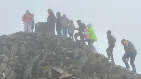 A line of people waiting to reach the trig point at the peak of Yr Wyddfa on a misty day