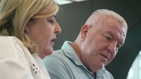 A middle ages man and woman sit side by side. They are both looking down. 