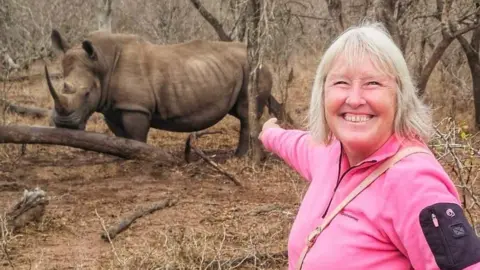 Lynn Stephenson wearing pink and pointing at a rhinoceros 