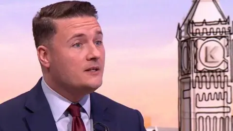 Wes Streeting has short brown hair, is clean shaven and has a white shirt, burgundy coloured tie and blue jacket.