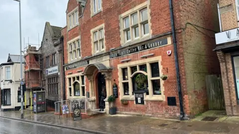 Andrew Turner/BBC The grand facade of the former HSBC/Midland Bank in Gorleston, featuring red brickwork and sandstone mullions around the windows and an arched portico at the entrance