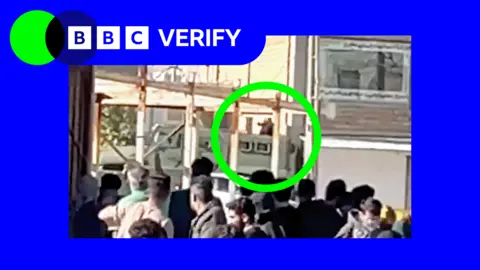 BBC A green circle highlighting an uniformed armed person on top of armoured vehicle point a gun near crowds gathered in Abdanan, Iran.