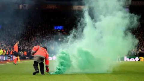 Reuters A football steward collects a green smoke bomb from a football pitch