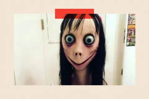 Social Media An image of the Momo image showing a young woman with long black hair, huge bulging eyes and a huge mouth with a big smile.