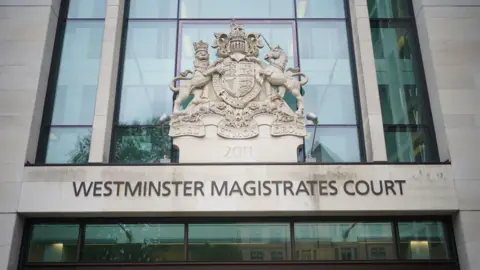 Yui Mok/PA Wire The entrance to Westminster Magistrates' Court, which has its name printed on the building. The building is a light colour with large glass windows.