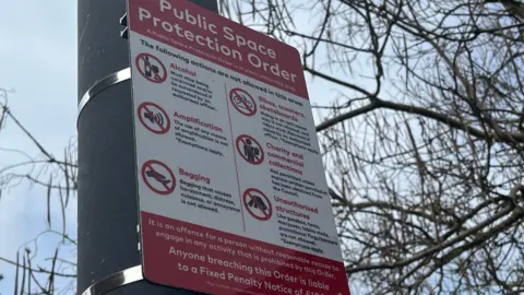 A red and white sign on a lamp post explaining the public space protection order rules.