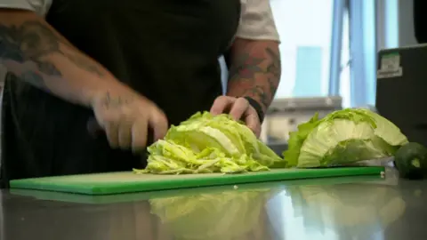 A chef slicing an iceberg lettuce in a kitchen.