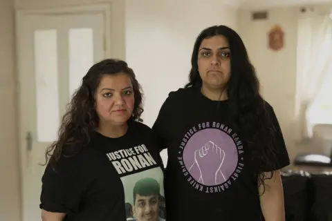 Pooja Kanda is wearing a black T-shirt with the words Justice for Ronan and a photo of her son who was killed in a sword attack. Her daughter Nikita stands next to her wearing a T-shirt saying: Justice for Ronan Kanda, fight against knife crime.