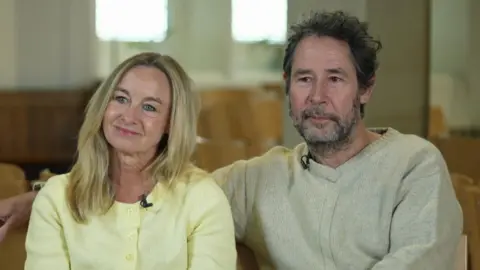 Rachel with long blonde hair wearing a yellow cardigan and Hamish next to her with short dark hair and a cream-coloured jumper.