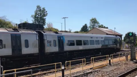 A South Western Railway train alongside the tracks on a sunny day.