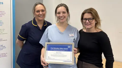OUH Sharon Andrews (Head of Midwifery, L) and Milica Redfearn (Director of Midwifery, R) stand either side of Maddy Ellison - who is holding up her certificate.