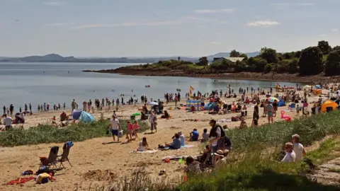 Many people sit on towels at the Silver Sands beach at Aberdour on a sunny day