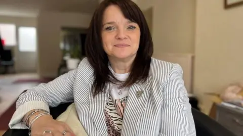 Buffy Williams pictured wearing a striped jacket and a t-shirt, with a house out of focus in the background.