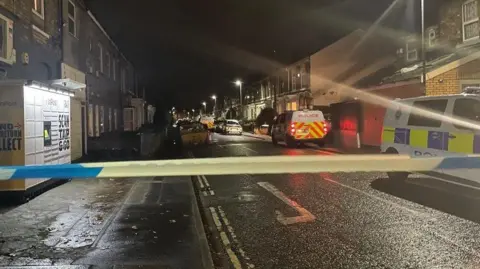 Police cordon and two police vans in a dark residential street.