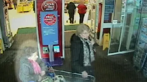 Cambridgeshire Police Una Crown is dressed in a grey coat with a pink scarf. She is pushing a shopping trolley assisted by another woman in a dark coat and grey scarf. They are in a supermarket lobby.