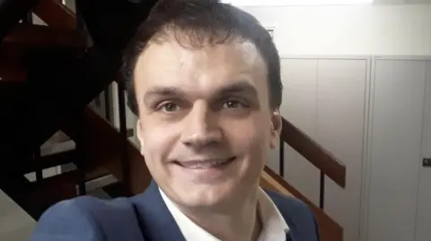 Reform UK A selfie of Paul Maginnis smiling and wearing a navy jacket and white collared shirt.