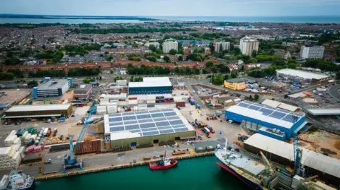 An aerial shot of Portsmouth International Port an area with boats, cranes and warehouse facilities and the city in the background