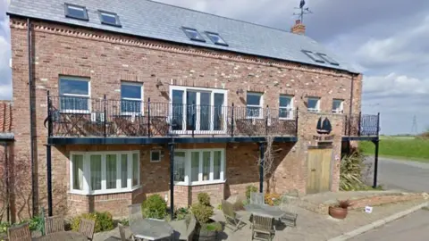 The brick work on the building is neat and give the appearance of a new building. It has a balcony on the second floor that runs along the length of the building. There is a logo of a black ship abover the wooden entrance door.