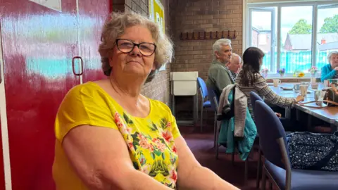 LDRS woman in a yellow t-shirt with grey hair and glasses.