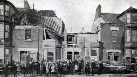 Hartlepool Museum and Gallery Service A black and white photograph of people trying to clear up rubble on Cleveland Road in Hartlepool after the bombardment. There is a house in the middle with its roof torn off and another one on the left with a collapsed  roof.