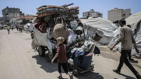 A young boy and adult man walk alongside a large trailer filled with belongings in Gaza City. A horse is pulling the large trailer